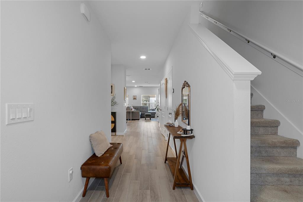 A hallway with wood-look tile flooring leads to a living area past a staircase — 5002 RAIN SHADOW DRIVE, ST CLOUD, FL