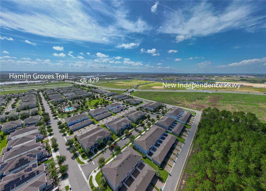 An aerial view shows a residential neighborhood with townhomes adjacent to a highway and forest — 6208 ARALIA IVY LANE, WINTER GARDEN, FL