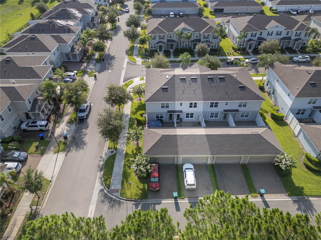 An aerial view shows a residential neighborhood with multi-story townhomes, paved streets, and parked cars — 6208 ARALIA IVY LANE, WINTER GARDEN, FL