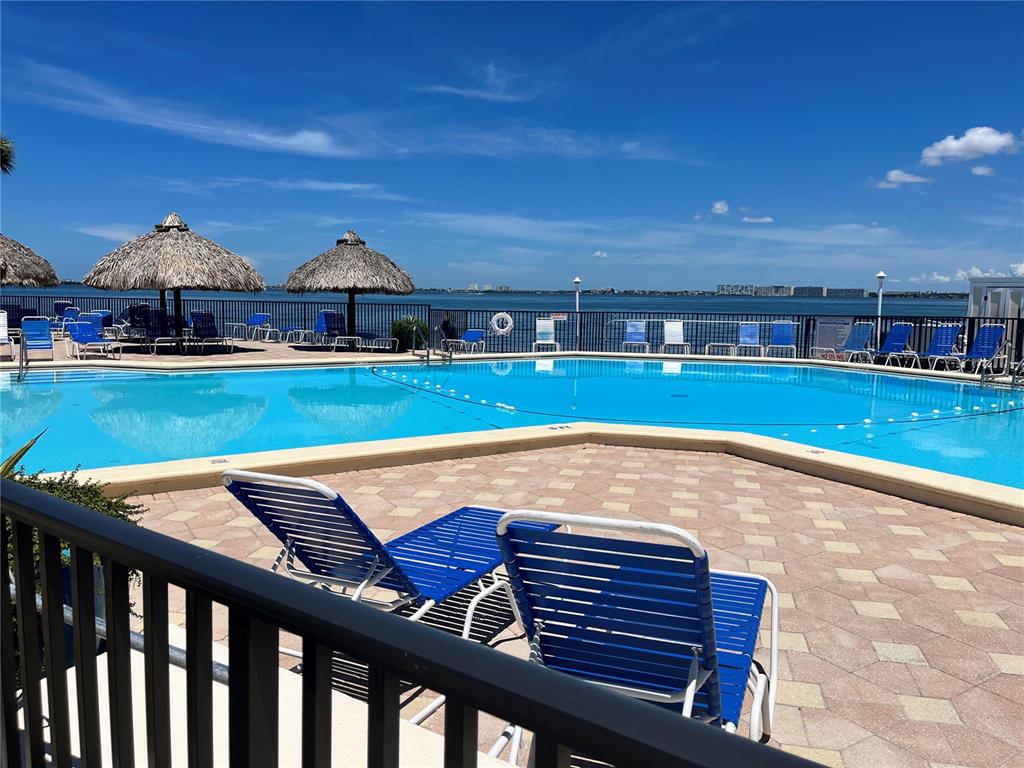 A swimming pool with lounge chairs and tiki umbrellas overlooks a bay under a blue sky — 5541 PUERTA DEL SOL BOULEVARD S UNIT 118, ST PETERSBURG, FL