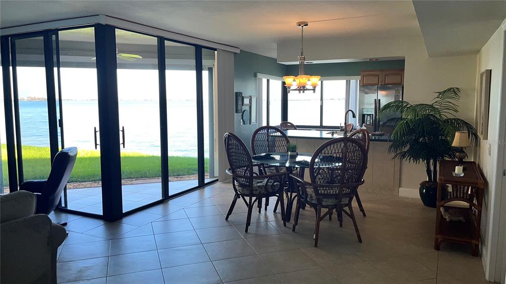 A dining area with wicker chairs overlooks a waterfront view through large glass sliding doors — 5541 PUERTA DEL SOL BOULEVARD S UNIT 118, ST PETERSBURG, FL