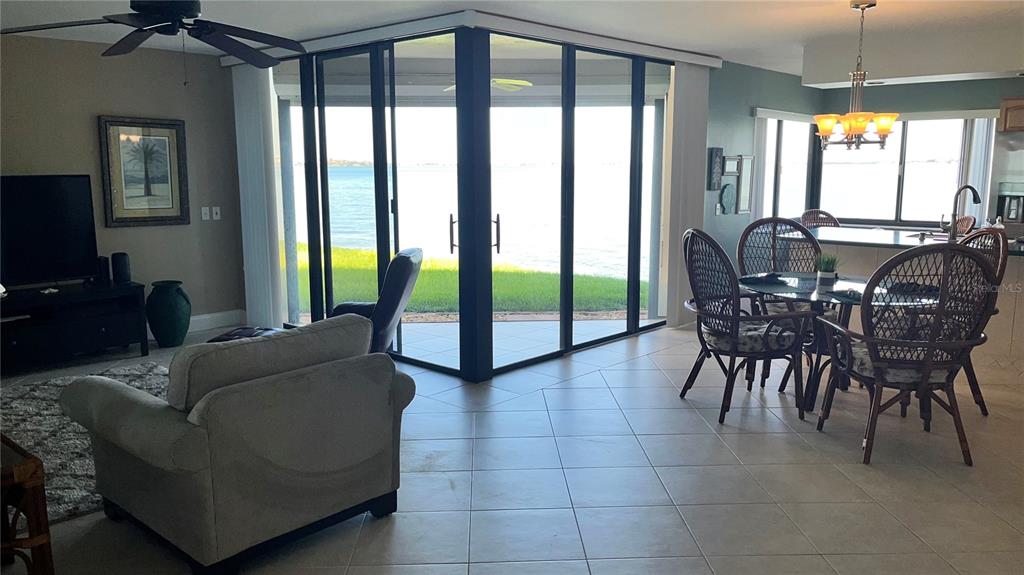 A living and dining area features tile floors, wicker chairs, and floor-to-ceiling windows overlooking water — 5541 PUERTA DEL SOL BOULEVARD S UNIT 118, ST PETERSBURG, FL
