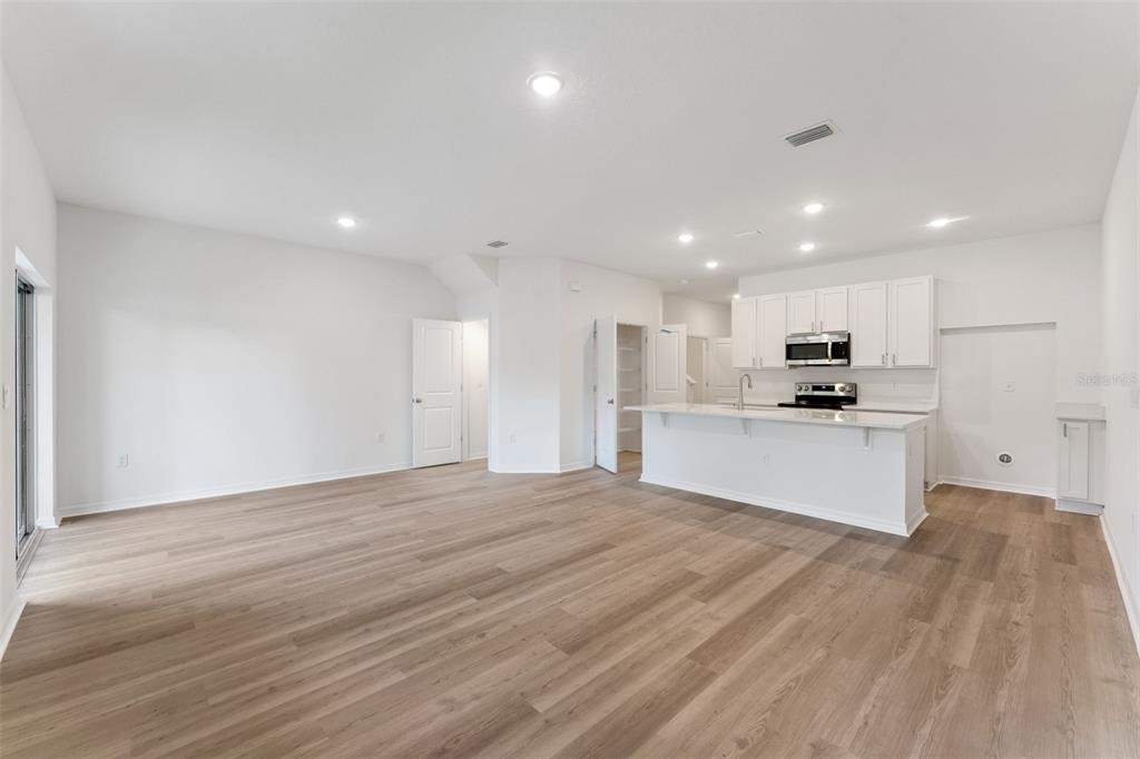 An open-concept kitchen and living area featuring white cabinetry, a kitchen island, and wood-look flooring — 646 CEDAR ELM COURT, EUSTIS, FL