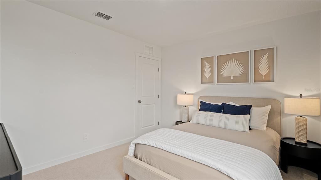 A bedroom features a bed with neutral bedding, two bedside lamps, and framed wall art — 6111 SWAMP BAY DRIVE, EDGEWATER, FL