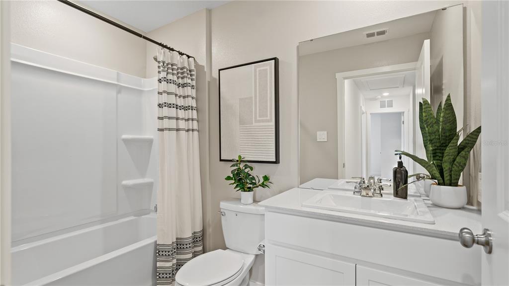 A bathroom features a white vanity, a toilet, and a shower-tub combination with a patterned curtain — 6111 SWAMP BAY DRIVE, EDGEWATER, FL