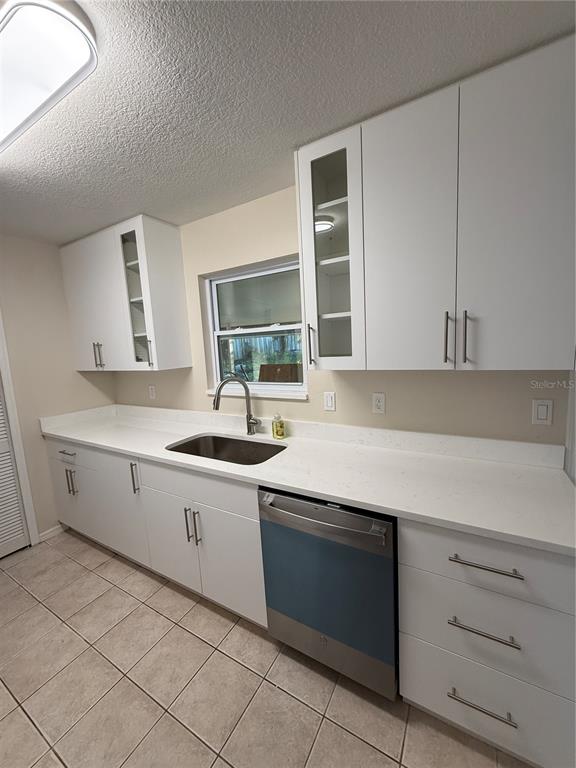 A kitchen features white cabinets, a stainless steel dishwasher, a sink, and light-colored tile flooring — 5454 BRACKEN COURT, WINTER PARK, FL