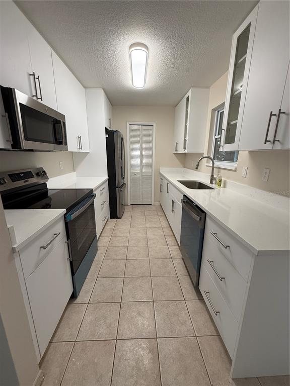 A galley kitchen features white cabinets, stainless steel appliances, quartz countertops, and tiled flooring — 5454 BRACKEN COURT, WINTER PARK, FL