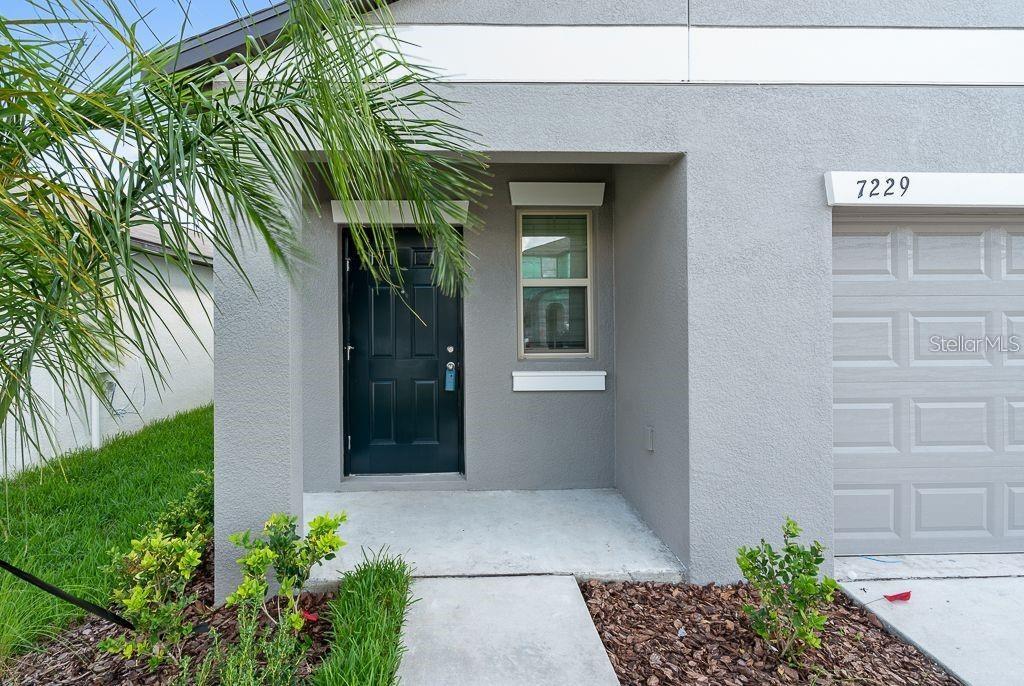 A gray house exterior features a dark front door, a single window, and a garage — 7229 SALT RIVER AVENUE, SUN CITY CENTER, FL