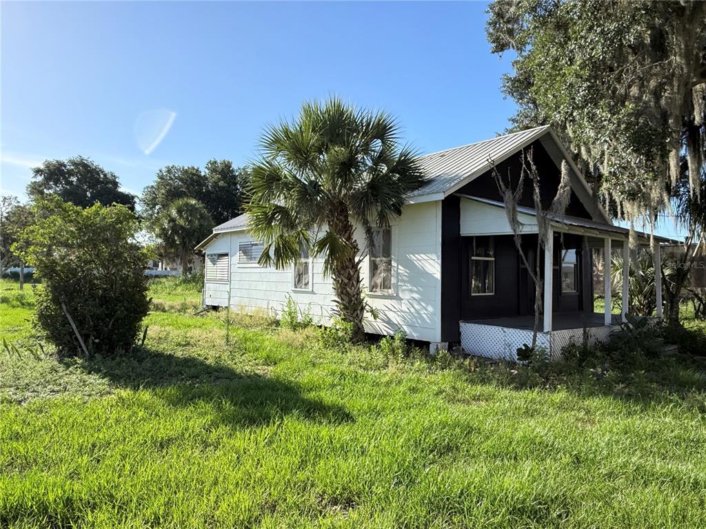 A white house with a dark porch and a metal roof sits in a grassy yard — 1015 MAKOWSKI ROAD, WAUCHULA, FL