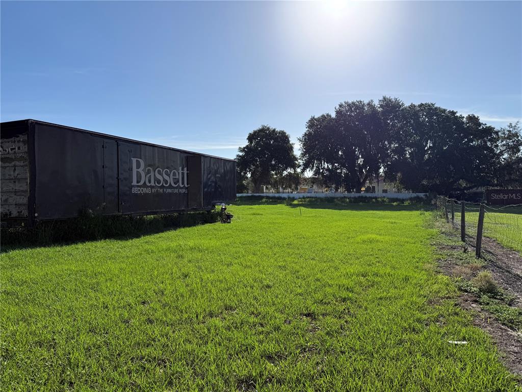 A large Bassett storage trailer sits on a grassy, fenced-in vacant lot under a bright sky — 1015 MAKOWSKI ROAD, WAUCHULA, FL
