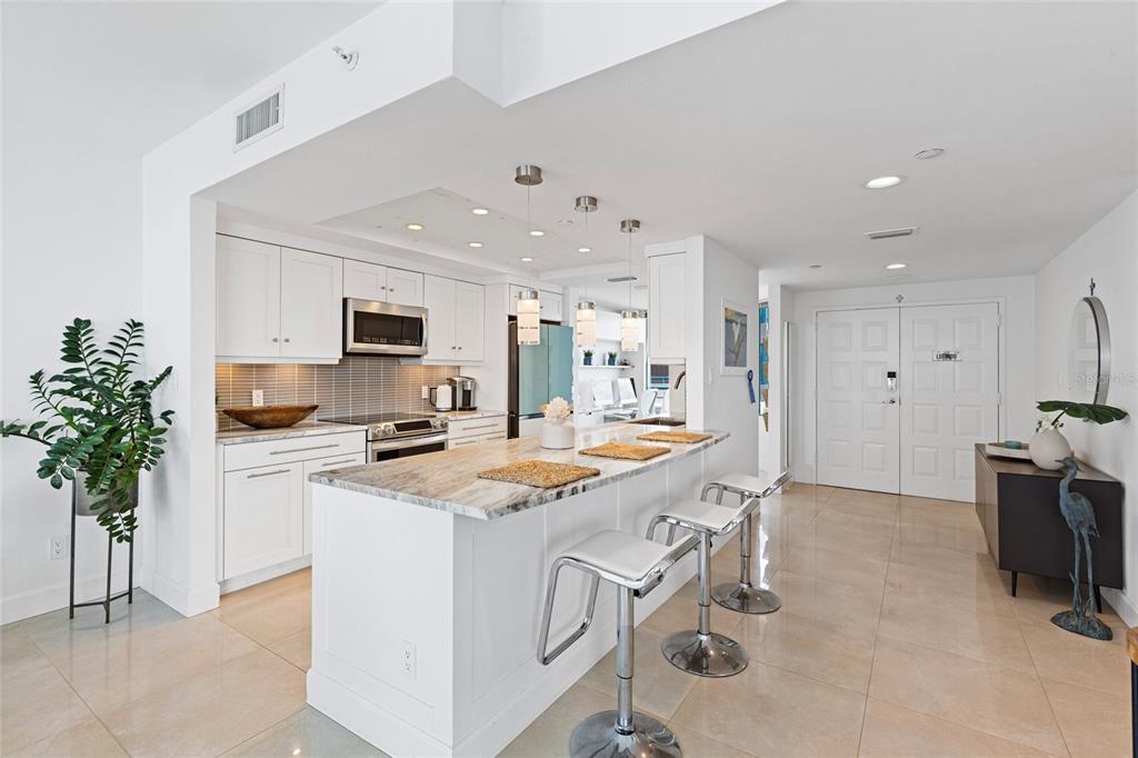 A bright, open-concept living area features a kitchen island with bar stools and tile flooring — 1520 GULF BOULEVARD UNIT 1807, CLEARWATER BEACH, FL