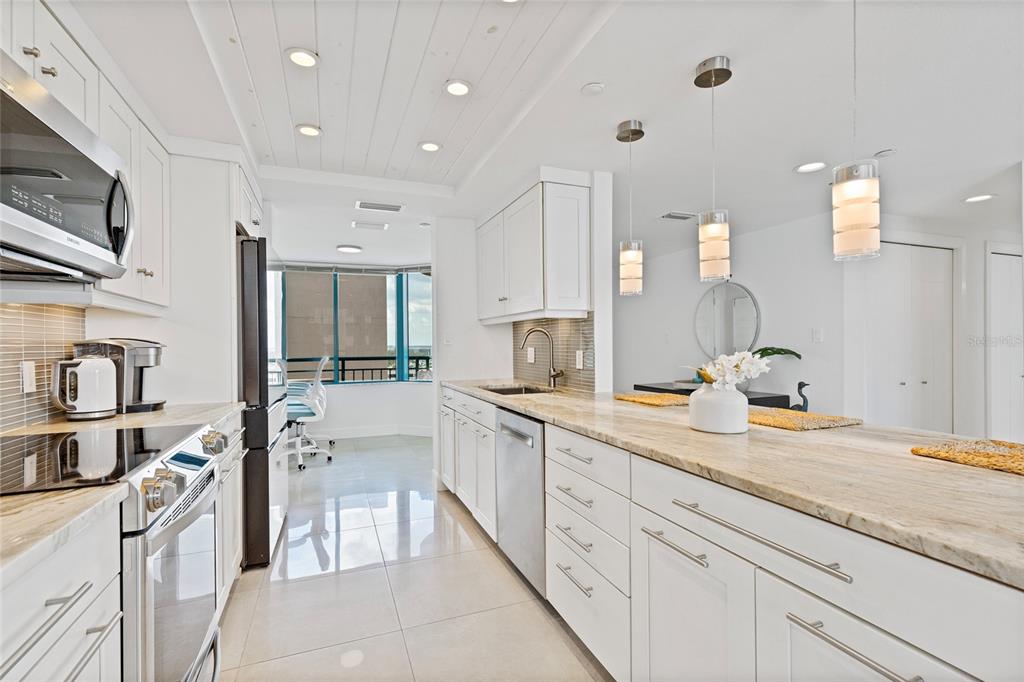 A modern kitchen features white cabinetry, a marble-topped island with bar stools, and tile flooring — 1520 GULF BOULEVARD UNIT 1807, CLEARWATER BEACH, FL