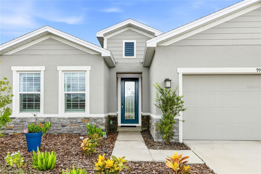 The exterior of a gray house features a blue front door and a stone-accented base — 9916 DAYBREAK GLEN, PARRISH, FL