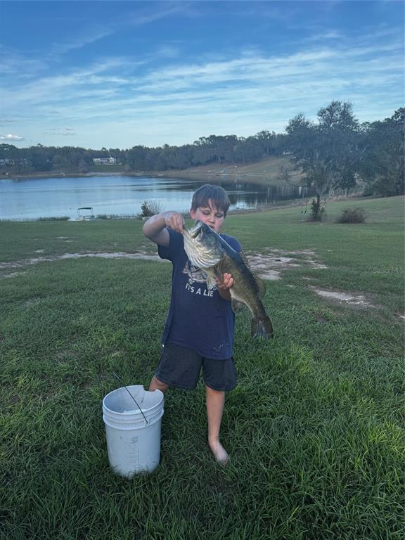 A young boy stands in a grassy field holding a large fish near a lake — 10615 SE 142ND AVENUE ROAD, OCKLAWAHA, FL