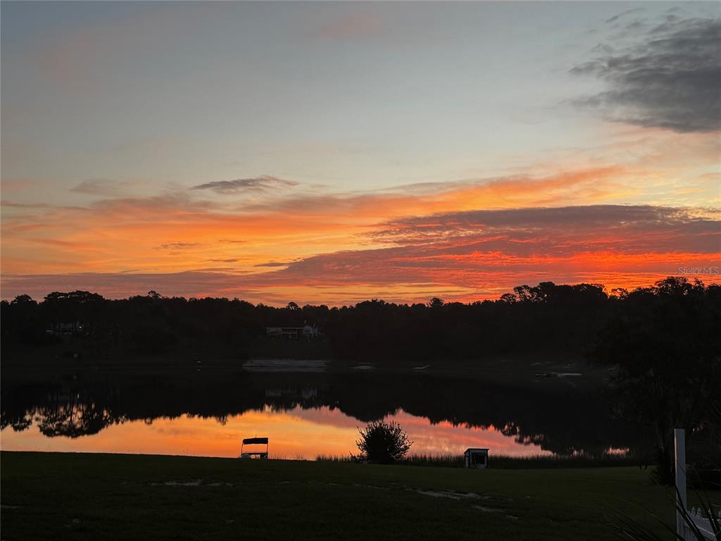 A vibrant sunset reflects over a calm lake with a grassy shoreline and distant trees — 10615 SE 142ND AVENUE ROAD, OCKLAWAHA, FL