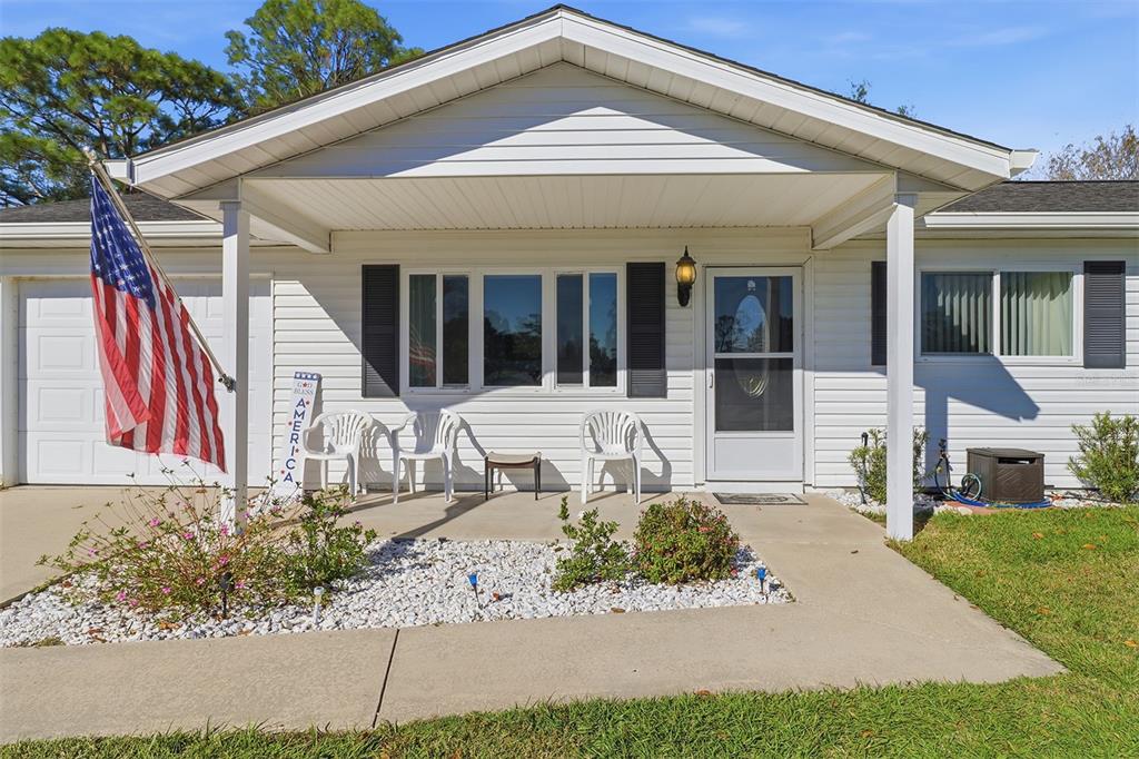 A white single-story house with a covered front porch, an American flag, and landscaping — 8571 SW 105TH PLACE, OCALA, FL