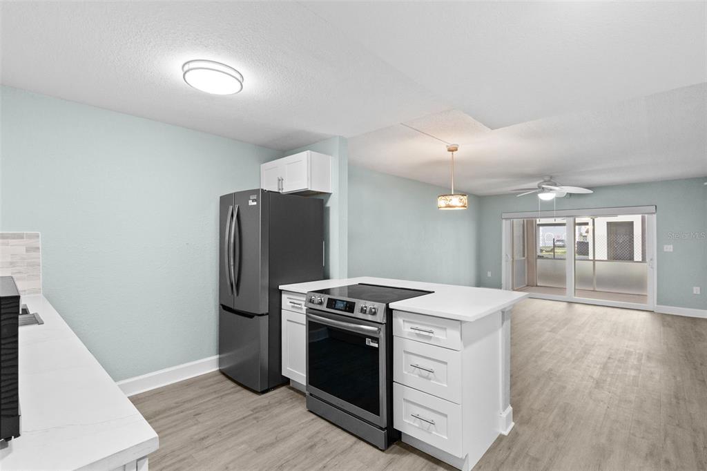 A kitchen with white cabinets, quartz countertops, and stainless steel appliances opens to a living area — 17035 GULF BOULEVARD UNIT 116, NORTH REDINGTON BEACH, FL