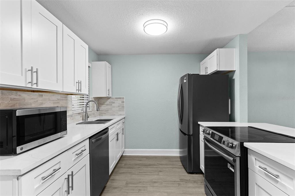 A kitchen features white cabinets, stainless steel appliances, a light backsplash, and wood-look flooring — 17035 GULF BOULEVARD UNIT 116, NORTH REDINGTON BEACH, FL