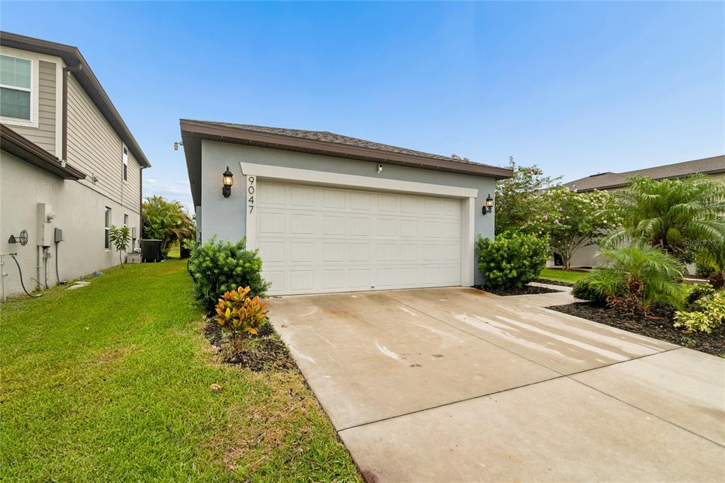 A covered front porch features a blue door with a patriotic wreath and surrounding landscaping — 9047 ROYAL RIVER CIRCLE, PARRISH, FL