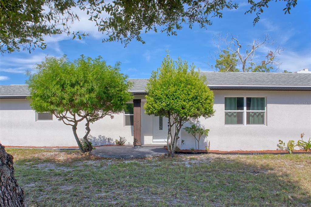 A single-story house with a white stucco exterior, a gray shingled roof, and two trees — 1301 WOODBINE STREET, CLEARWATER, FL