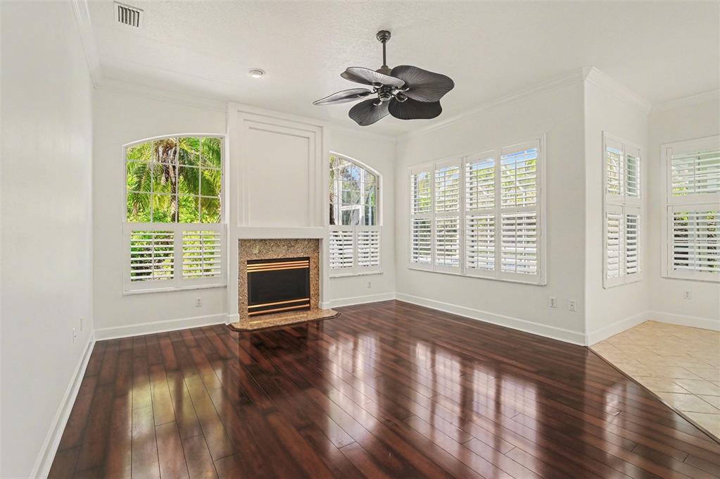 An empty living room features dark hardwood floors, a fireplace, and white plantation shutters — 8 FOX CLIFF WAY, ORMOND BEACH, FL