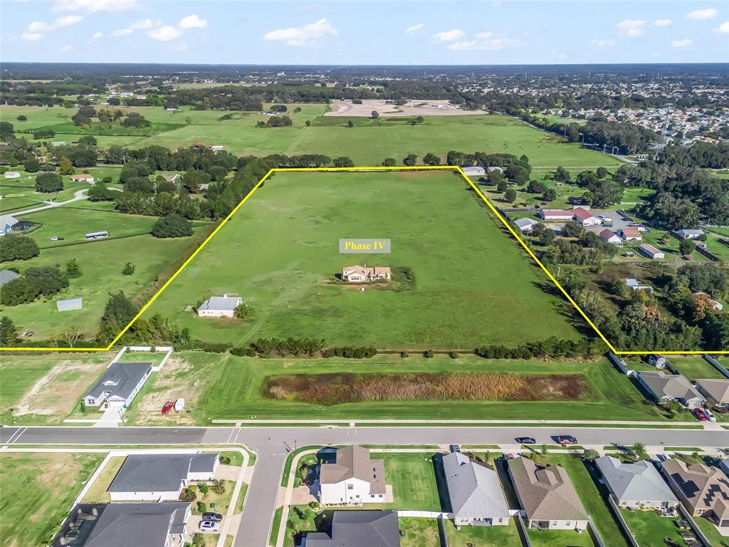 An aerial view shows a large, rectangular grassy lot outlined in yellow behind residential homes — NE 125TH LOOP, PHASE 4, OXFORD, FL