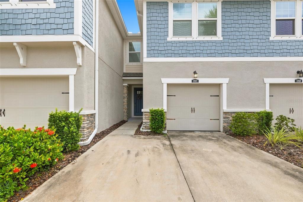 A view of a townhouse exterior featuring a concrete driveway, garage doors, and blue siding — 17871 STELLA MOON PLACE, LUTZ, FL