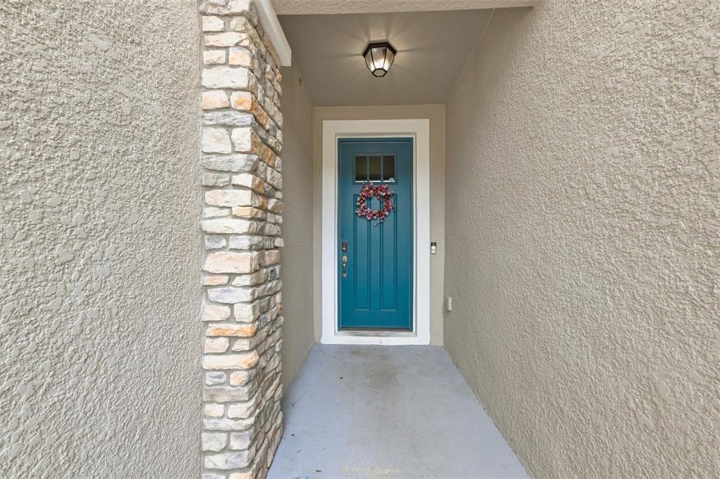 A teal front door with a wreath sits at the end of a covered entryway — 17871 STELLA MOON PLACE, LUTZ, FL