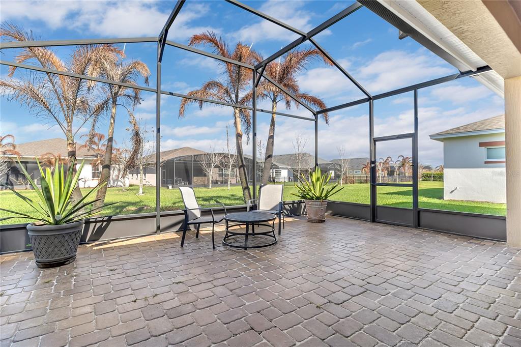 A screened-in patio features a paver floor, two chairs, a small table, and potted plants — 5017 E FOUNTAINWOOD DRIVE, ST CLOUD, FL