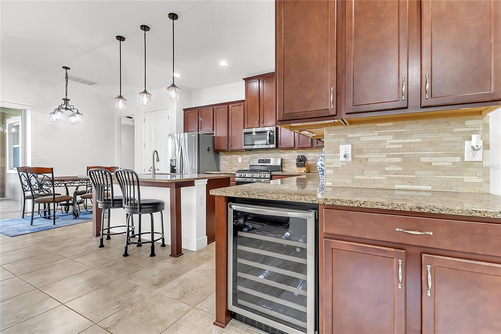A kitchen features dark wood cabinets, granite countertops, a wine cooler, and a dining area — 5017 E FOUNTAINWOOD DRIVE, ST CLOUD, FL