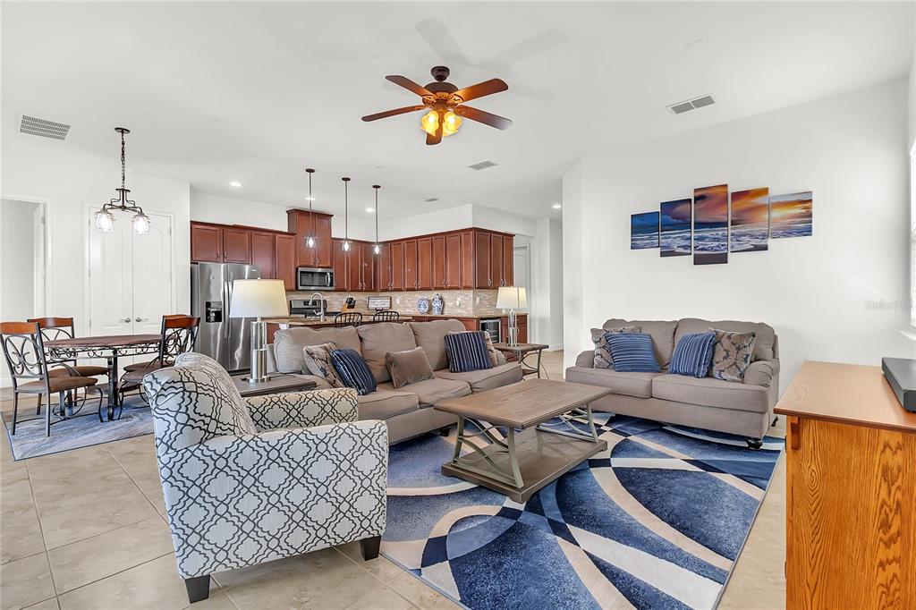 An open-concept living room and kitchen feature tile floors, wood cabinetry, and blue area rugs — 5017 E FOUNTAINWOOD DRIVE, ST CLOUD, FL