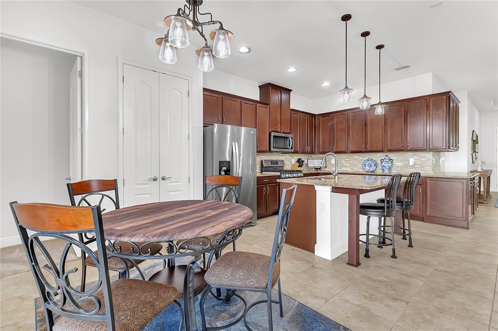 A kitchen with dark wood cabinets, granite countertops, and a dining area with a round table — 5017 E FOUNTAINWOOD DRIVE, ST CLOUD, FL