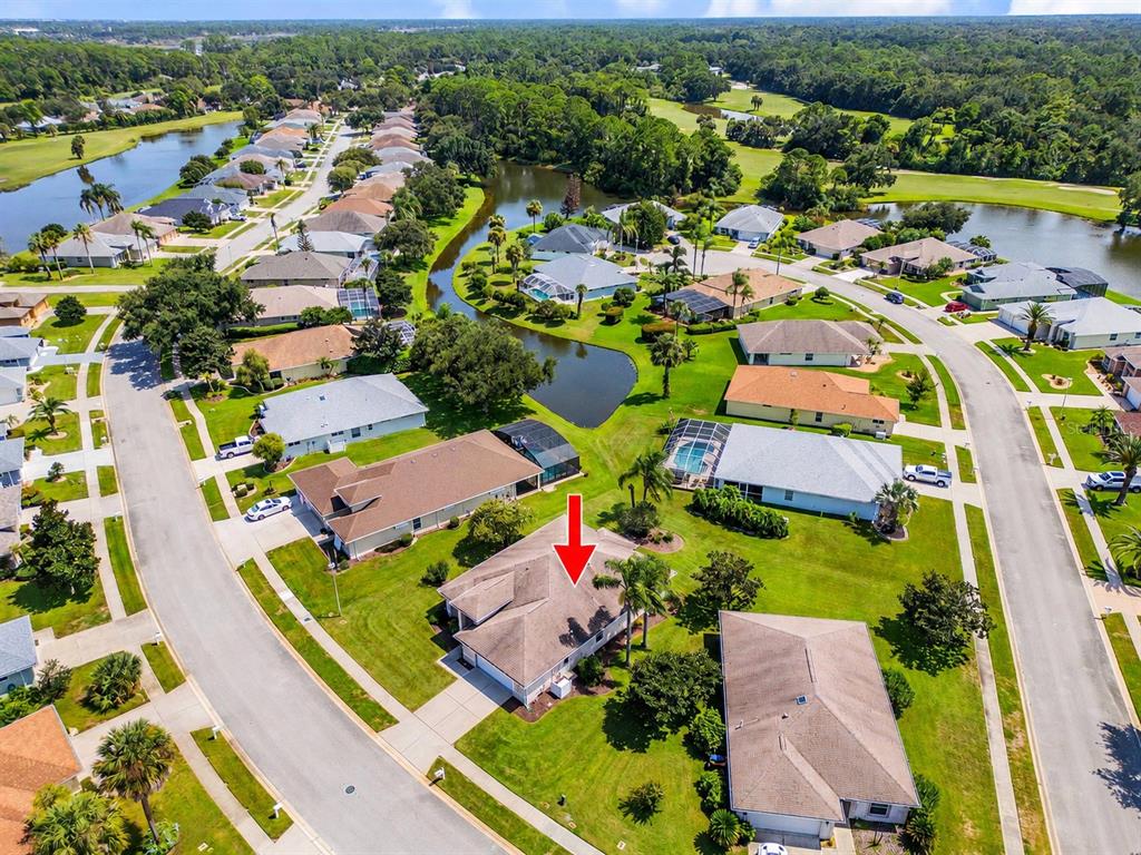 An aerial view shows a suburban neighborhood with houses, lawns, and a central pond — 1858 TURNBULL LAKES DRIVE, NEW SMYRNA BEACH, FL