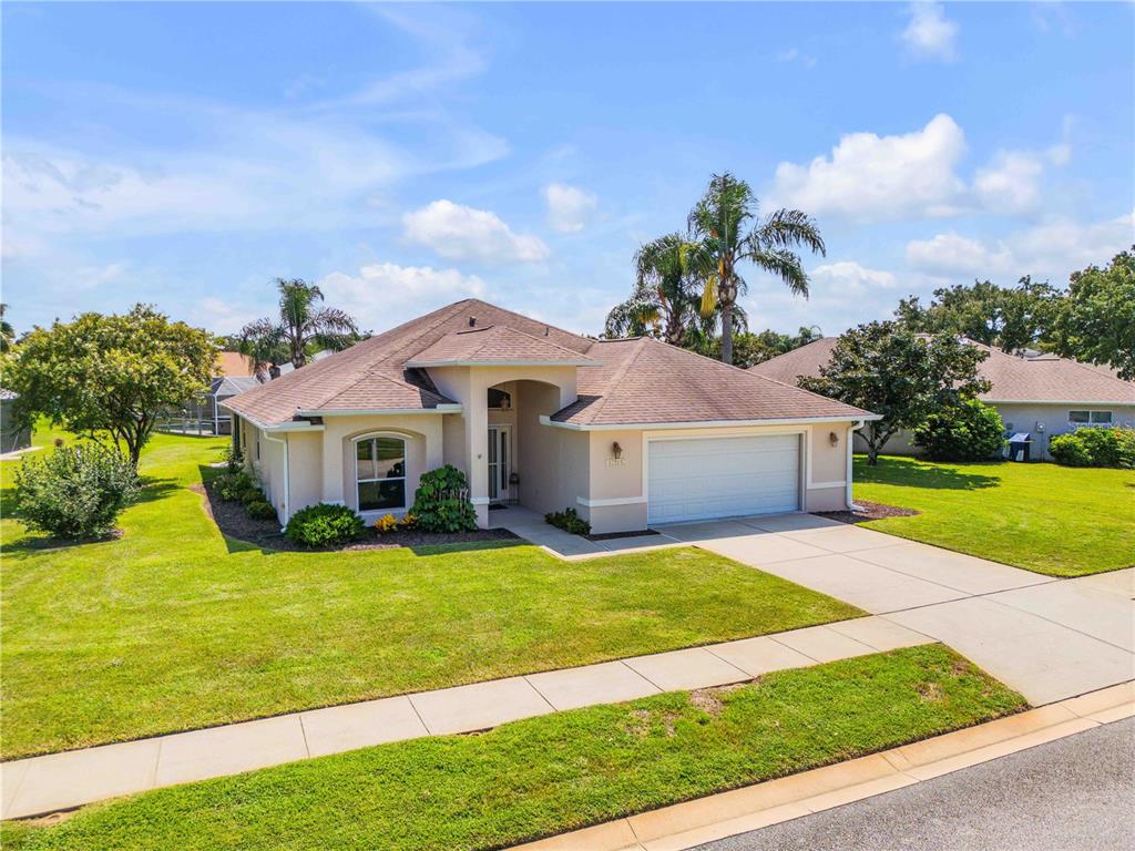 A single-story suburban house with a tan stucco exterior, a two-car garage, and a lawn — 1858 TURNBULL LAKES DRIVE, NEW SMYRNA BEACH, FL