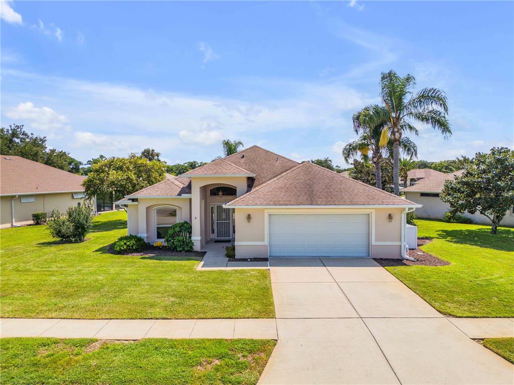 A single-story suburban house with a tan exterior, a two-car garage, and a palm tree — 1858 TURNBULL LAKES DRIVE, NEW SMYRNA BEACH, FL