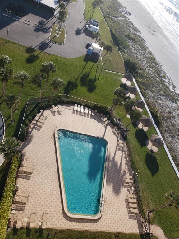 An aerial view shows a swimming pool with lounge chairs on a patio near the beach — 1460 GULF BOULEVARD UNIT 1102, CLEARWATER, FL