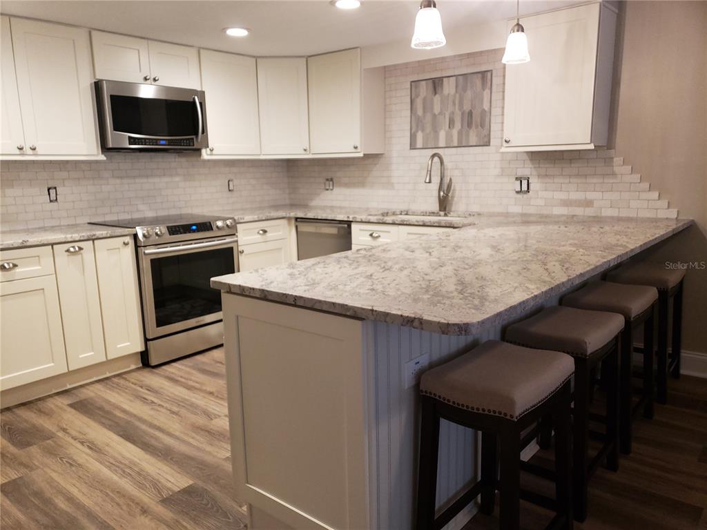 A kitchen features white cabinets, granite countertops, a subway tile backsplash, and a breakfast bar — 1460 GULF BOULEVARD UNIT 1102, CLEARWATER, FL