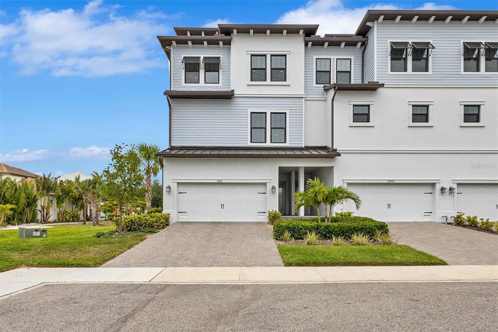 A three-story townhouse with a two-car garage and light-colored siding under a blue sky — 3027 BERMUDA SLOOP CIRCLE, RUSKIN, FL