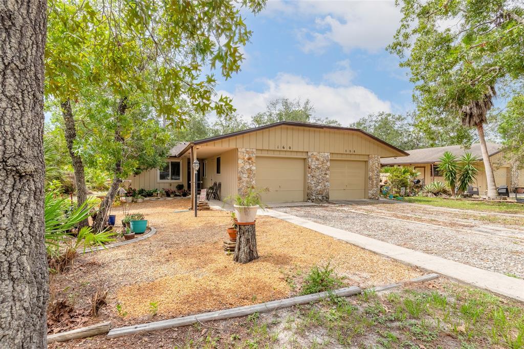 A single-story duplex with tan siding, stone accents, and two garage doors under a roof — 160 MAGNOLIA LOOP, PORT ORANGE, FL