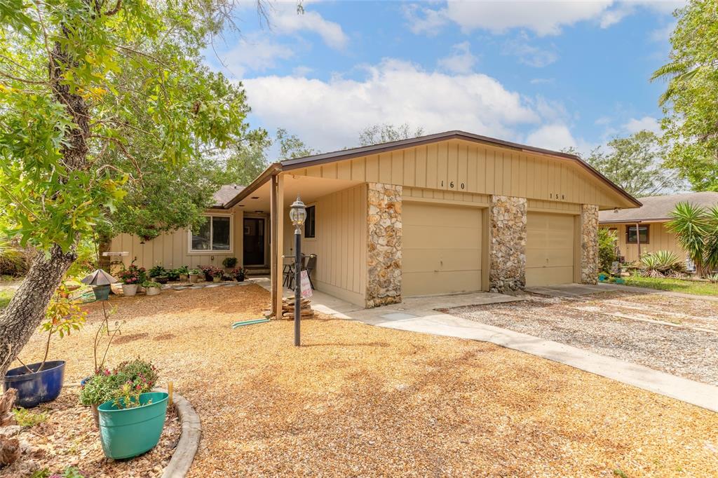 A single-story duplex with tan vertical siding, stone accents, and a gravel front yard — 160 MAGNOLIA LOOP, PORT ORANGE, FL