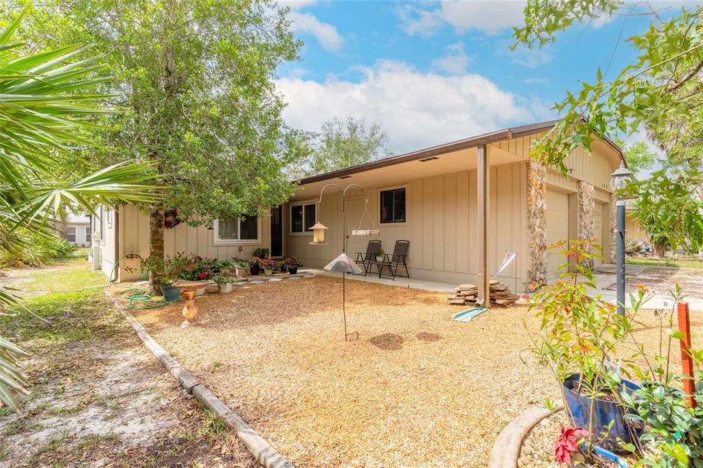 A tan house exterior features a gravel yard, a covered patio, and a stone pillar — 160 MAGNOLIA LOOP, PORT ORANGE, FL