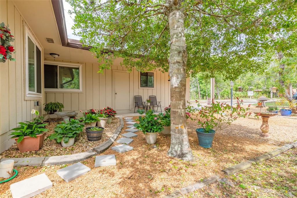A house exterior features a beige wall, a stone path, and potted plants under trees — 160 MAGNOLIA LOOP, PORT ORANGE, FL