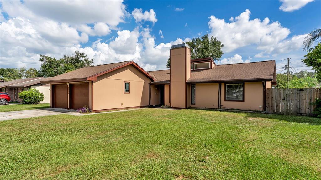 A tan single-story house with a two-car garage, a prominent chimney, and a wooden fence — 2236 COUNTRY LOOP N, LAKELAND, FL