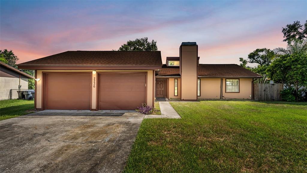 A single-story house with a two-car garage, a chimney, and a brown roof at sunset — 2236 COUNTRY LOOP N, LAKELAND, FL