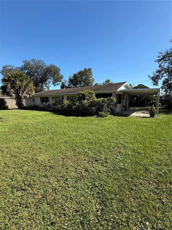 A single-story house with a carport sits behind a large, grassy yard — 1985 ALADDIN COURT, ST CLOUD, FL