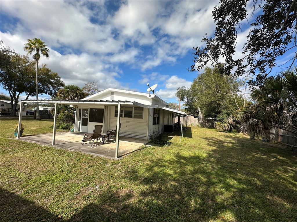 A white house with a covered concrete patio sits in a grassy backyard — 1985 ALADDIN COURT, ST CLOUD, FL