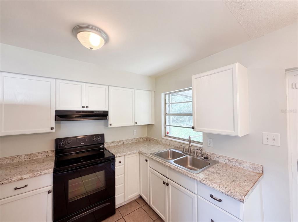 A kitchen with white cabinets, granite countertops, a black stove, and a double sink — 1735 JEFFERSON DRIVE, MOUNT DORA, FL