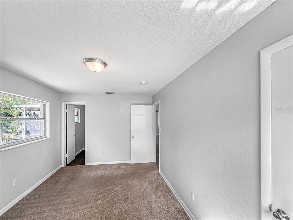 A bedroom with gray walls, brown carpet, a window, and two interior doors — 1735 JEFFERSON DRIVE, MOUNT DORA, FL