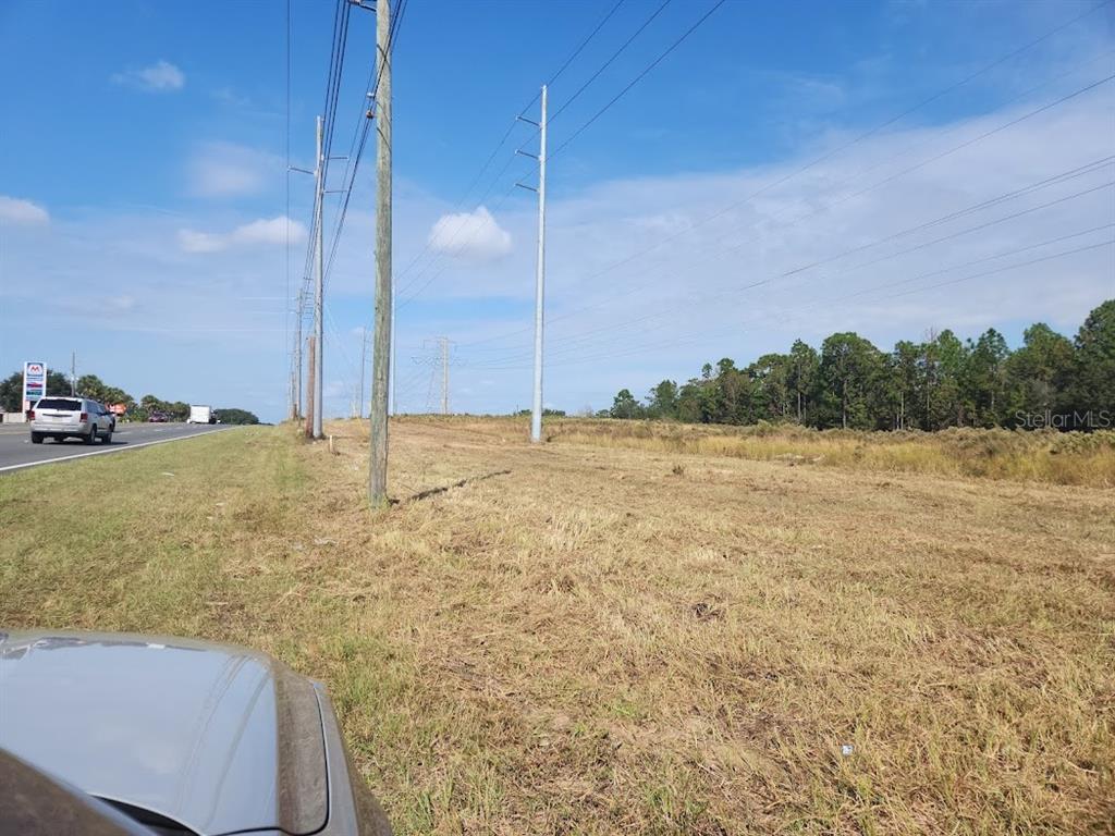 A grassy roadside lot features utility poles and power lines next to a highway — SE MARICAMP ROAD, OCALA, FL