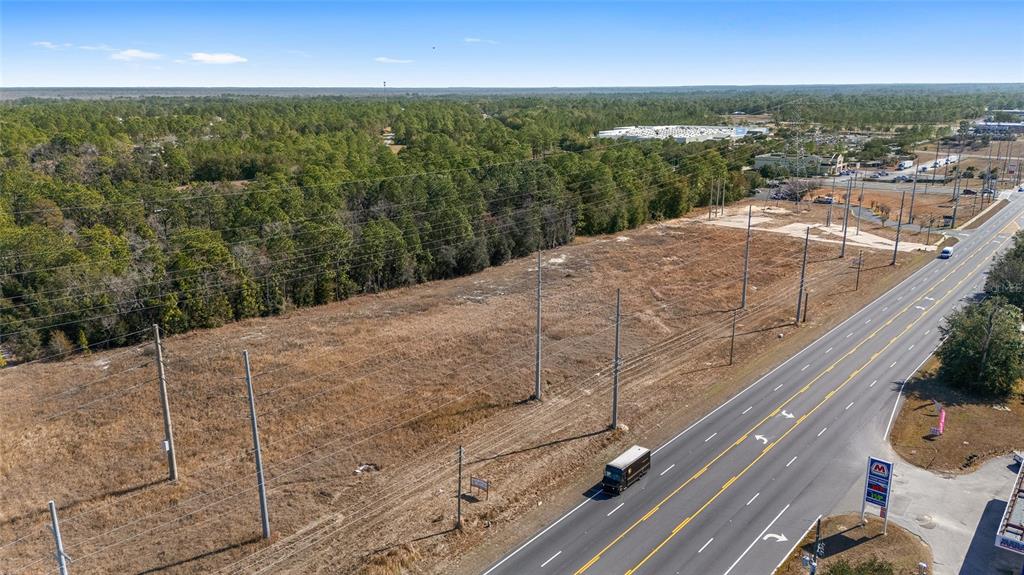 An aerial view shows a large, vacant grassy lot adjacent to a multi-lane highway — SE MARICAMP ROAD, OCALA, FL
